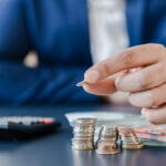 Businessman,Holding,Euro,Cents,Coins,Dollar,Bills,On,Table,With